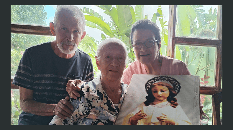 Foto LPG Marielos Román. Puro amor . Doña María junto a la imagen de la Virgen Niña, en compañía de  a su hermano  Mario (izquierda) y de su hermana  Marta (derecha).