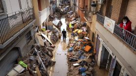 Varias personas caminan por una calle con muebles y escombros apilados a los lados de un área afectada por las inundaciones, en Paiporta, Valencia, España, el martes 5 de noviembre de 2024.